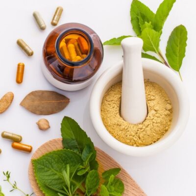 A bowl of yellow powder with a grinding tool, a capsule jar nearby, scattered capsules, and green leaves, symbolizing herbal and natural digestive support.