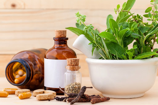 A bowl of green vegetables with a couple of jars, one laying on the table with capsules spilling out, symbolizing digestive health and natural healing.